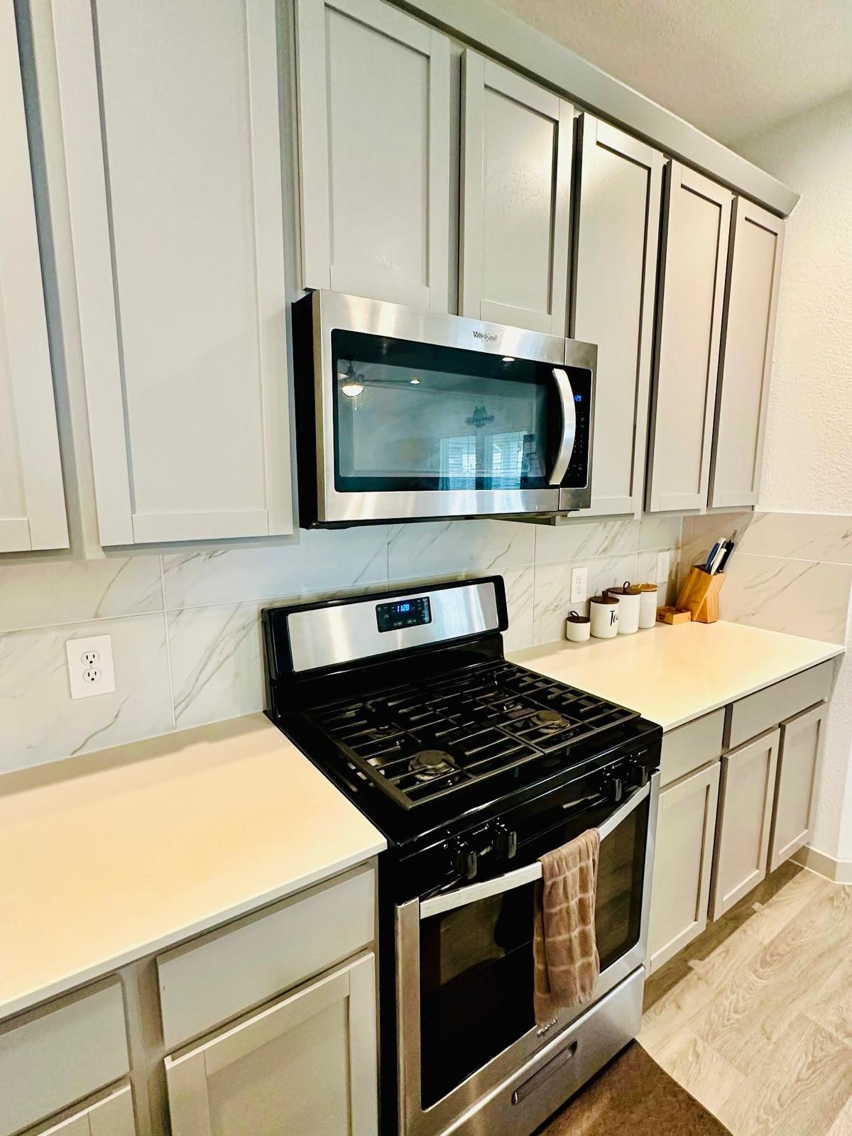 315 John House Lane Rosharon, TX 77583 - Photo 15 of 27 Modern kitchen with sleek light wood cabinets, a spacious island with a sink, and stainless steel appliances. The room features ample counter space, recessed lighting, and a stylish backsplash, creating a bright and inviting space for cooking and entertaining.