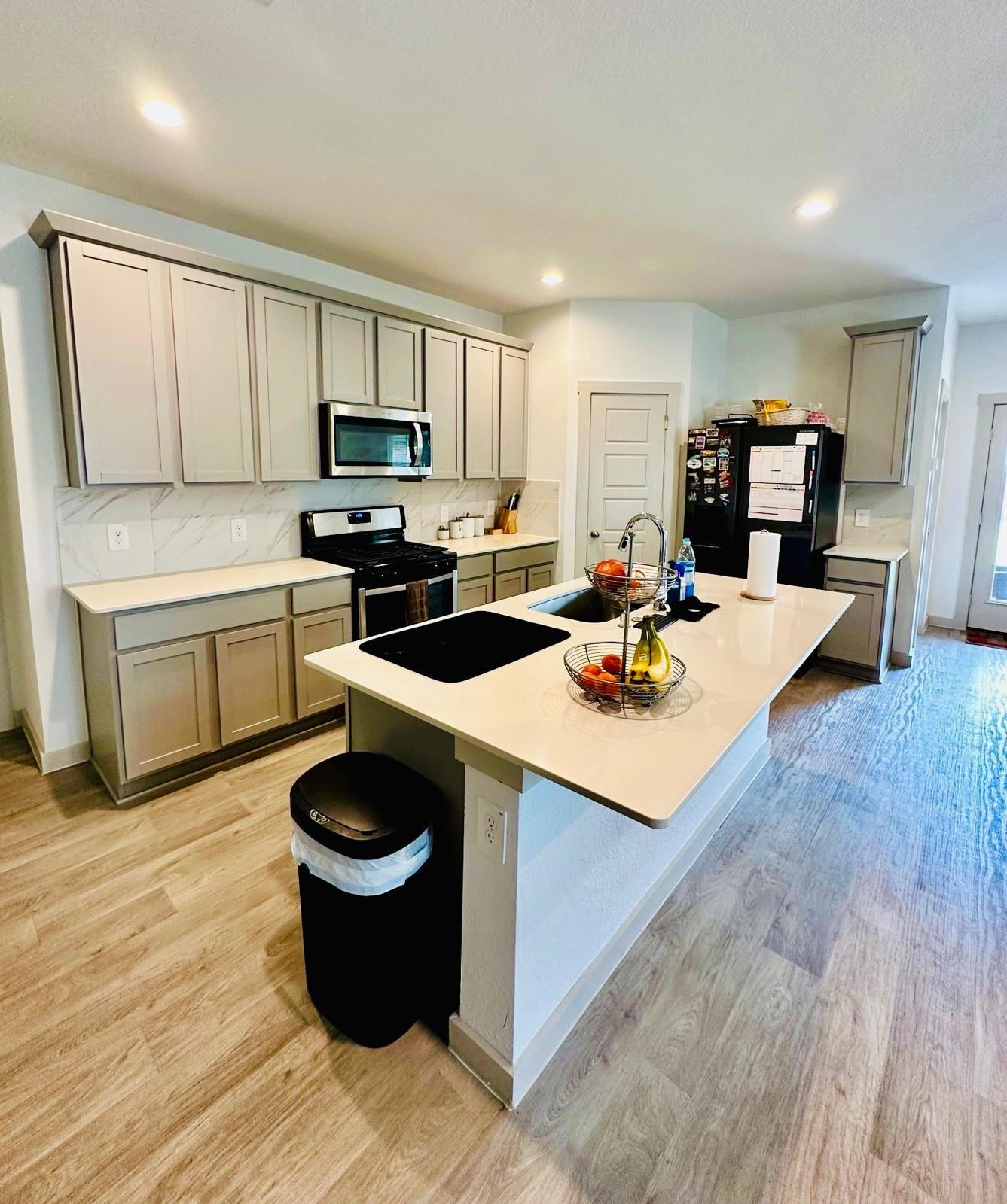 315 John House Lane Rosharon, TX 77583 - Photo 17 of 27 Modern kitchen with sleek light wood cabinets, a spacious island with a sink, and stainless steel appliances. The room features ample counter space, recessed lighting, and a stylish backsplash, creating a bright and inviting space for cooking and entertaining.