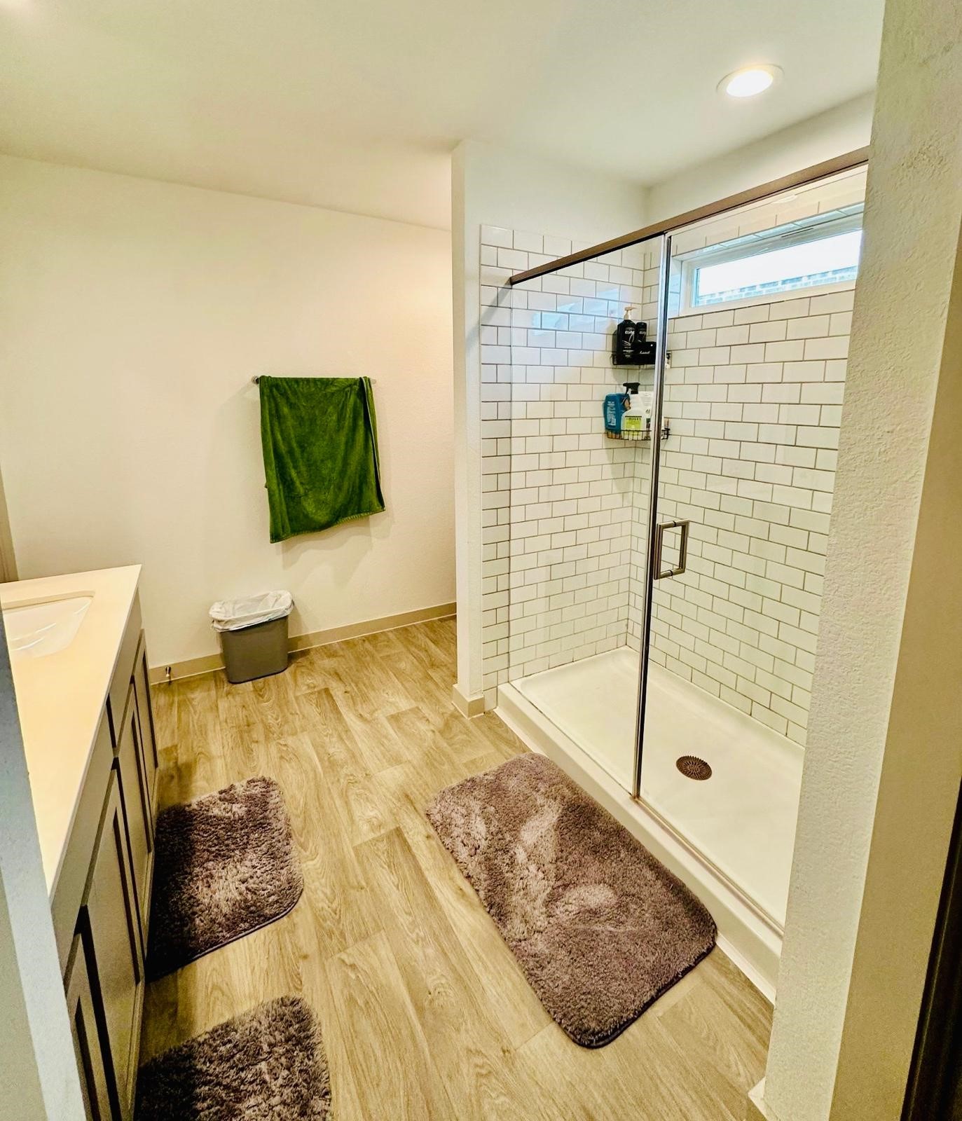 315 John House Lane Rosharon, TX 77583 - Photo 19 of 27 Bright bathroom with wood-style flooring, featuring a spacious glass-enclosed shower with subway tiles. Includes modern vanity and ample lighting.