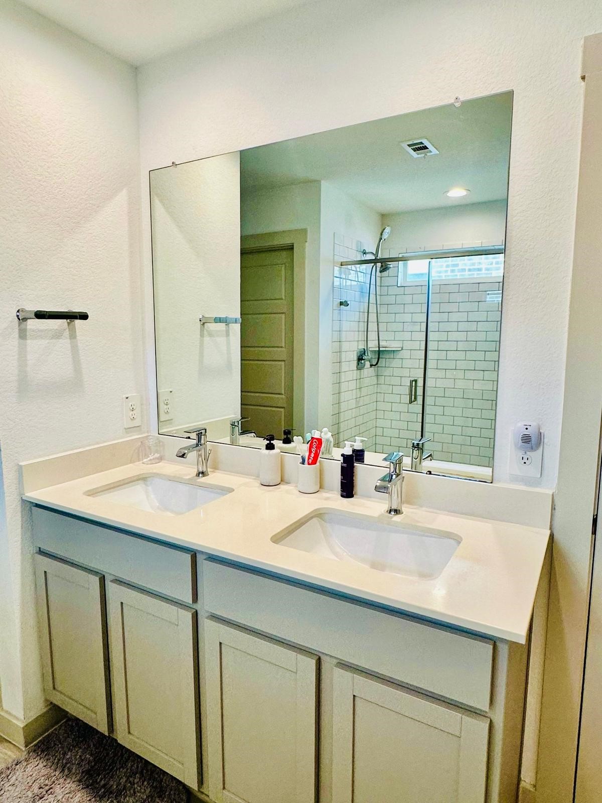 315 John House Lane Rosharon, TX 77583 - Photo 23 of 27 This photo shows a modern bathroom with a double vanity, large mirror, and a glass-enclosed shower with subway tile.