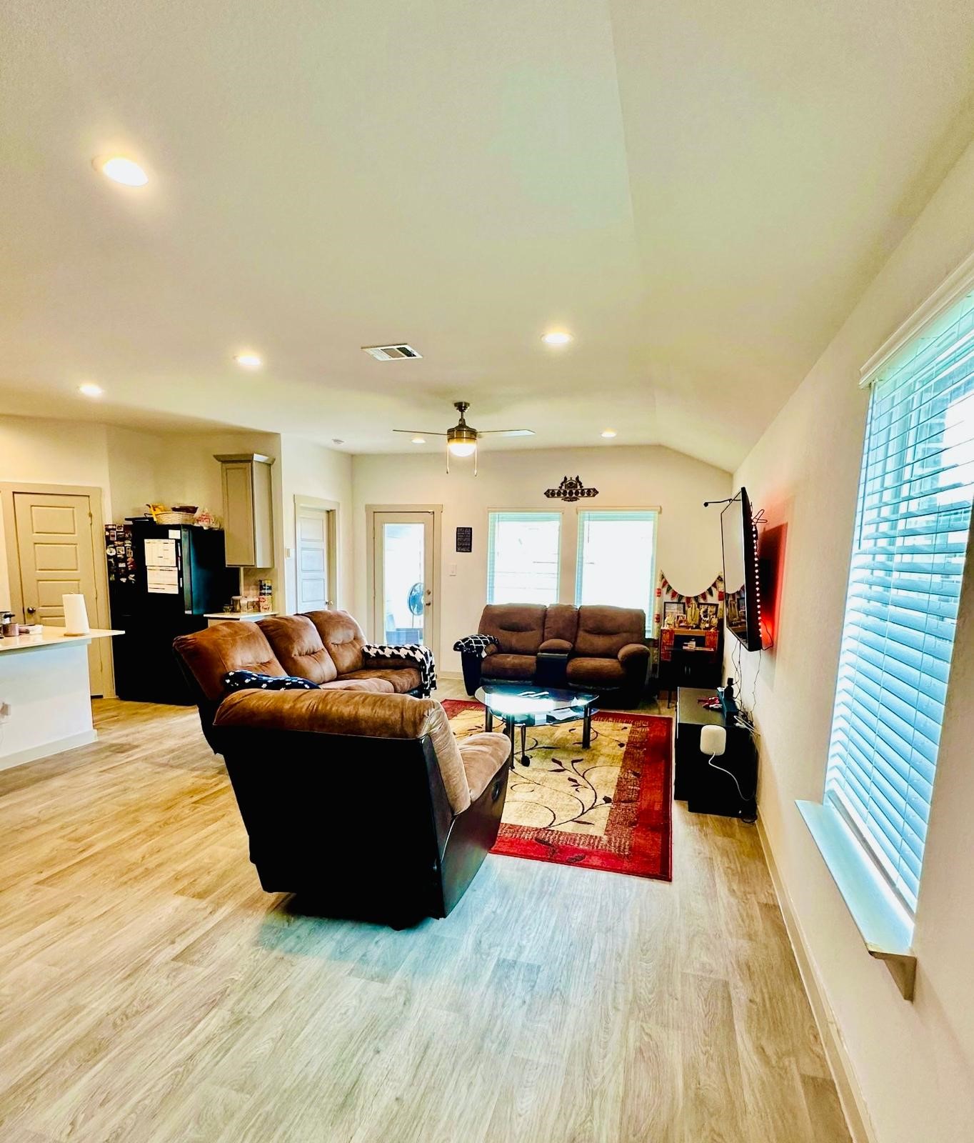 315 John House Lane Rosharon, TX 77583 - Photo 8 of 27 This welcoming living space features an open layout with modern wood flooring, ample natural light from large windows, and cozy seating. A mounted TV and adjacent kitchen area enhance functionality and comfort.