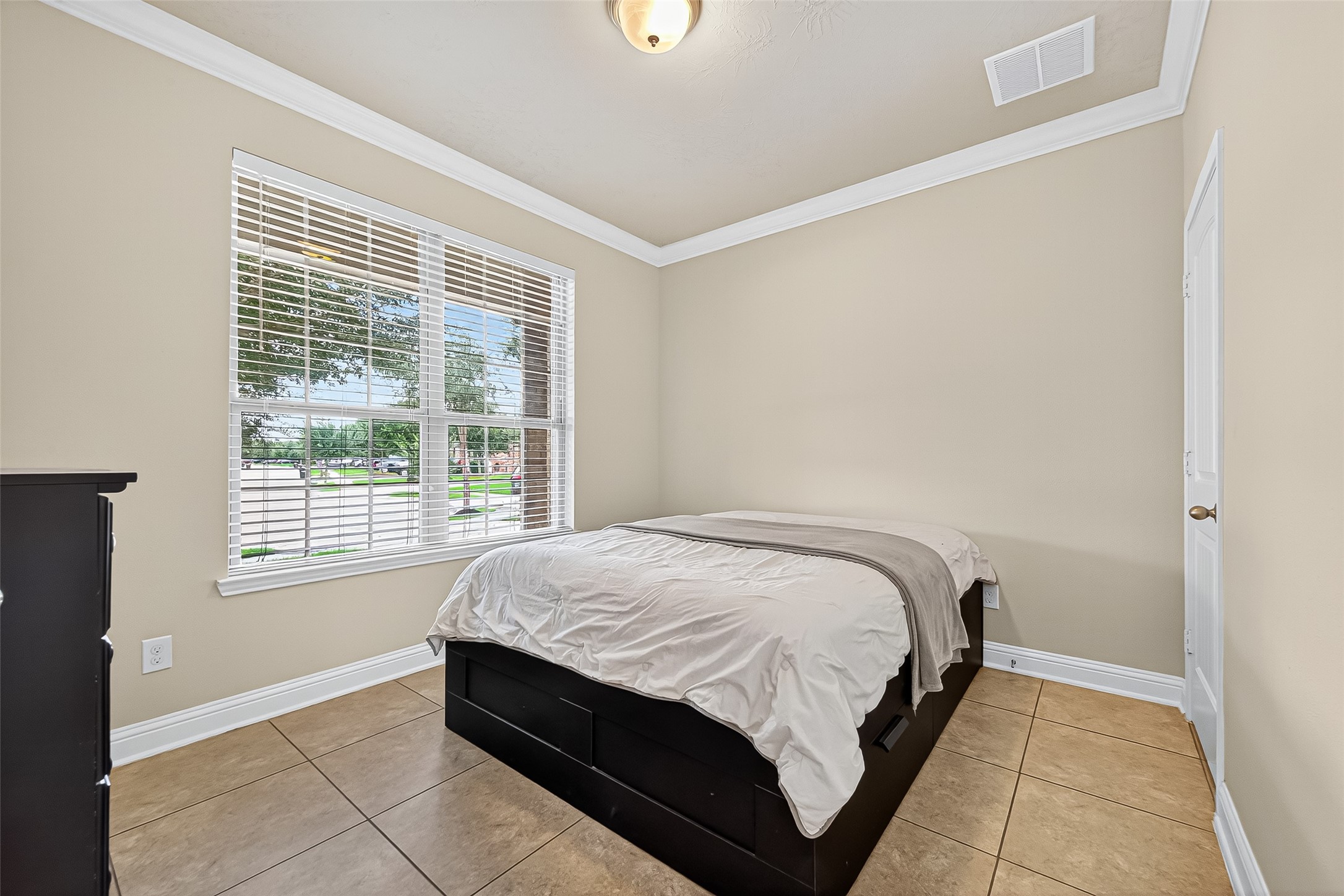 8107 Lockridge Terrace Lane Cypress, TX 77433 - Photo 24 of 50 This cozy downstairs bedroom is filled with natural light from large windows and offers a peaceful view of the front yard. With elegant crown molding and easy-to-maintain tile flooring, it’s perfect as a guest suite, home office, or multi-generational space with added privacy.