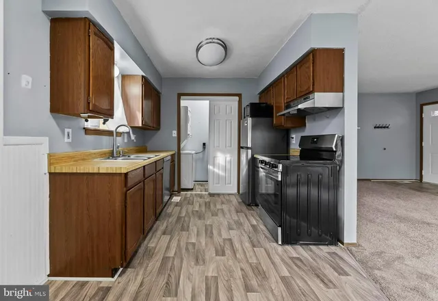 a kitchen with stainless steel appliances granite countertop a refrigerator a oven a sink with wooden cabinets and wooden floor