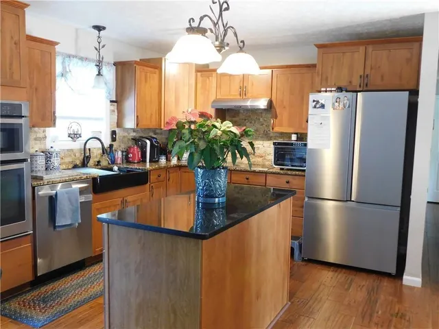 a kitchen with stainless steel appliances granite countertop a refrigerator a sink dishwasher a stove and a dining table with wooden floor