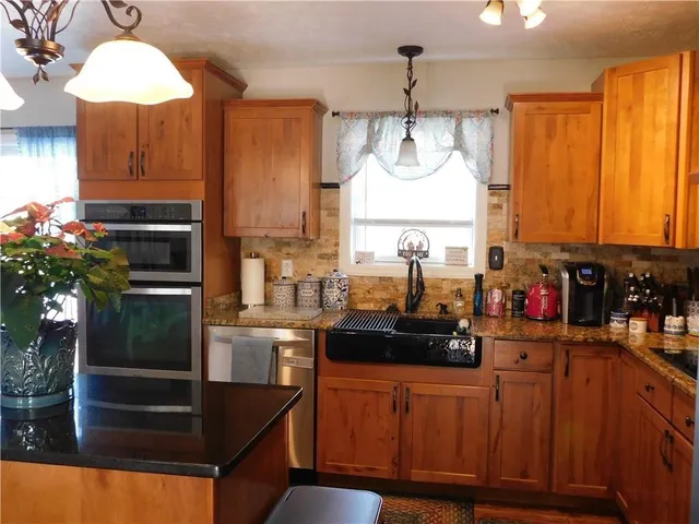 a kitchen with stainless steel appliances granite countertop a refrigerator a sink dishwasher a stove and a dining table with wooden floor