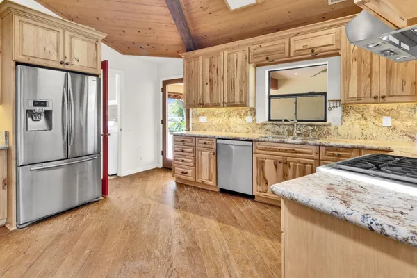 a kitchen with stainless steel appliances granite countertop a refrigerator a stove a sink and white cabinets with wooden floor
