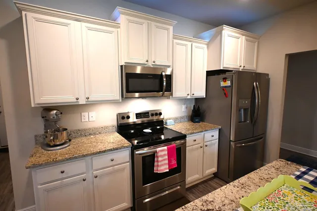 a kitchen with stainless steel appliances a stove a sink dishwasher a refrigerator with white cabinets and wooden floor