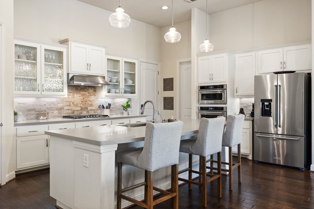 207 San Siro Cove Austin, TX 78738 - Photo 7 of 40 The kitchen showcases stainless steel appliances, elegant white cabinetry with glass-front accents, an eat-in breakfast bar, and a large island with built-in sink.