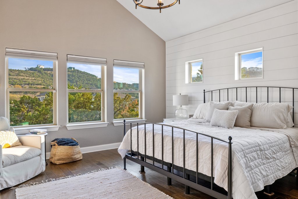 207 San Siro Cove Austin, TX 78738 - Photo 8 of 40 The spacious primary bedroom showcases a vaulted ceiling, wood floors, elegant suspended lighting, and breathtaking views of the hill country.