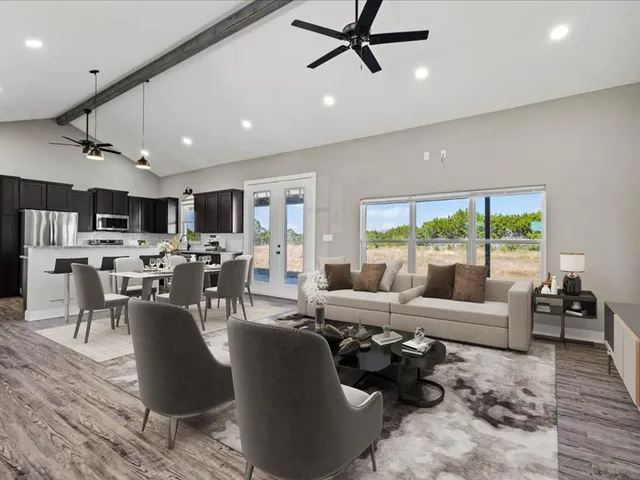 a living room with stainless steel appliances furniture large windows and wooden floor