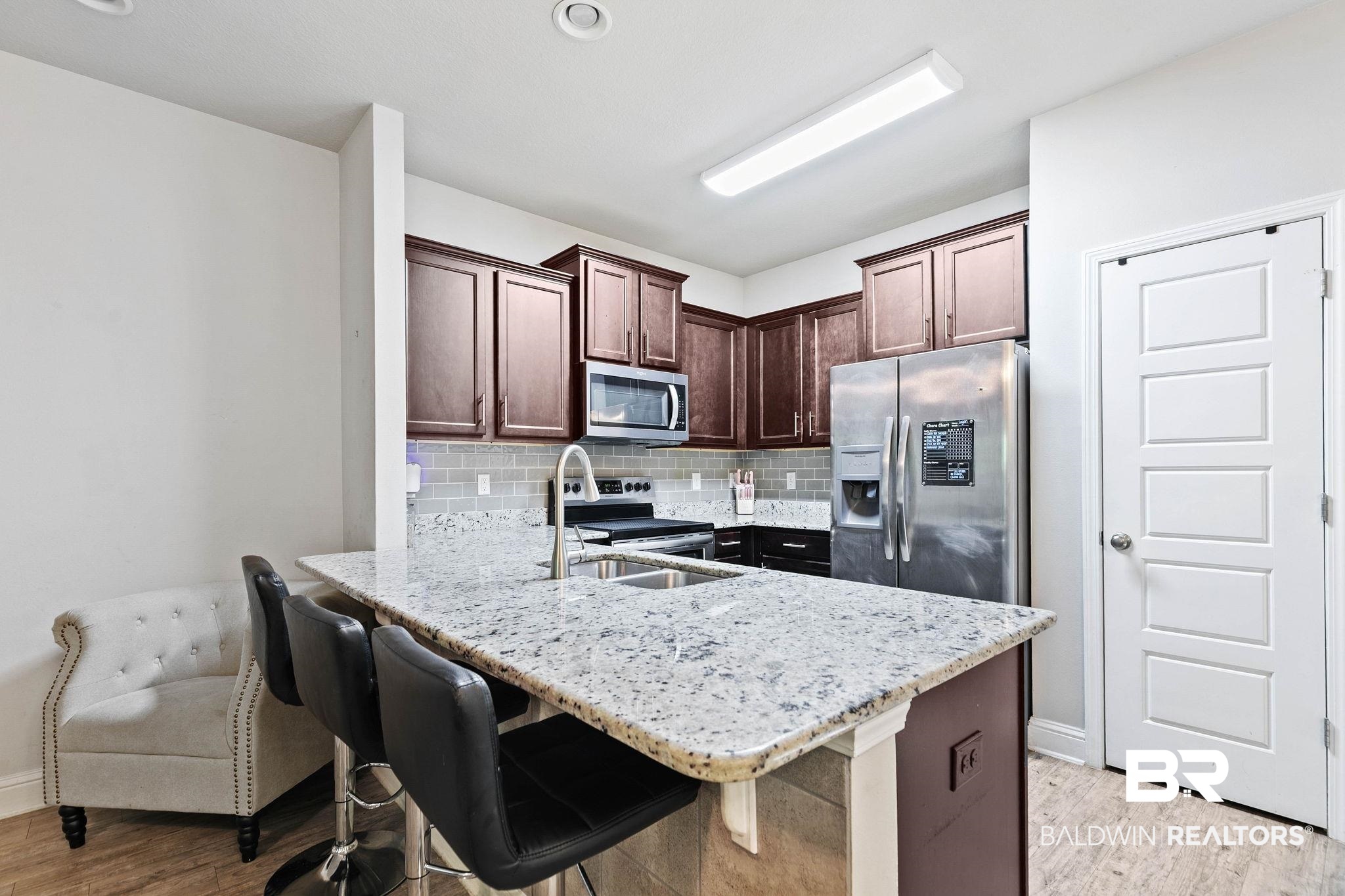 25806 Pollard Road, Unit 24 Daphne, AL 36526 - Photo 9 of 33 Kitchen featuring decorative backsplash, dark brown cabinetry, light wood-style flooring, and a peninsula