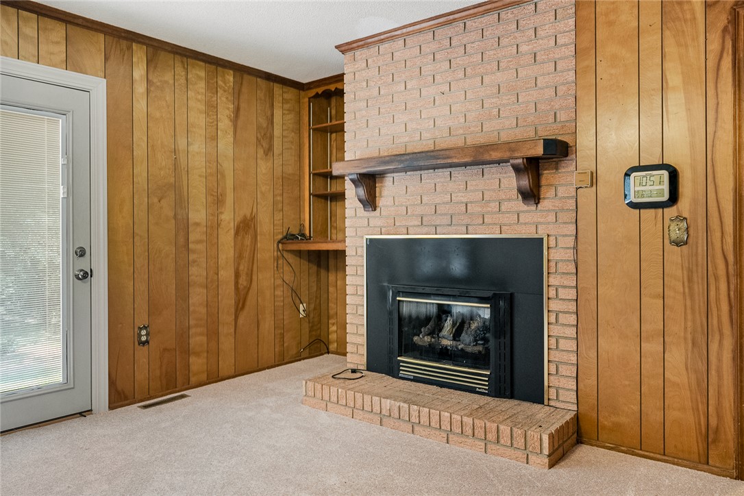 2101 Old Spring Drive Anderson, SC 29625 - Photo 8 of 36 A cozy living space features a brick fireplace with a mantle, complemented by wood paneling and plush carpeting.