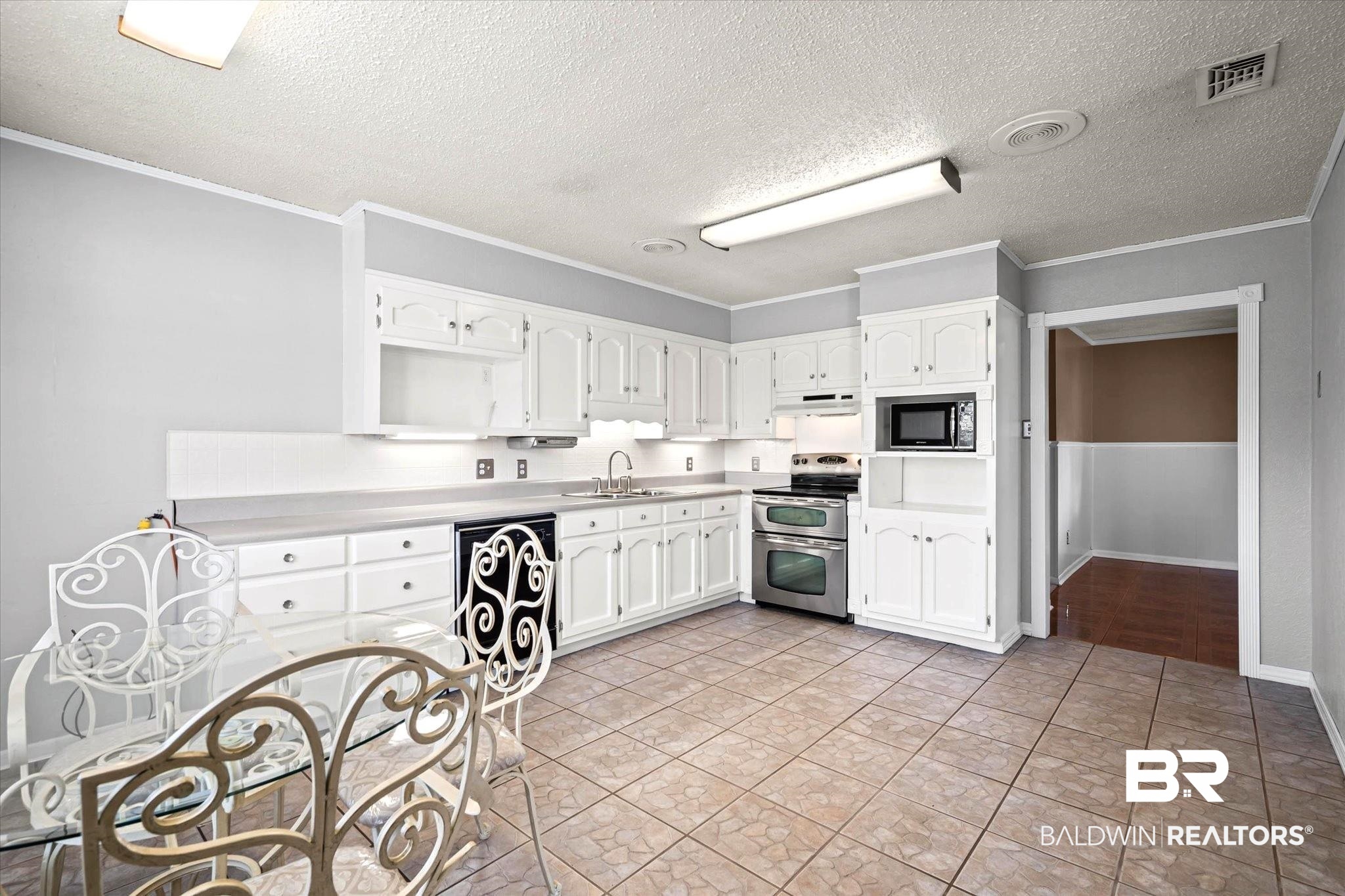 8090 Murray Hill Road Irvington, AL 36544 - Photo 15 of 40 Kitchen with white cabinets, oven range, light countertops, a textured ceiling, and ornamental molding