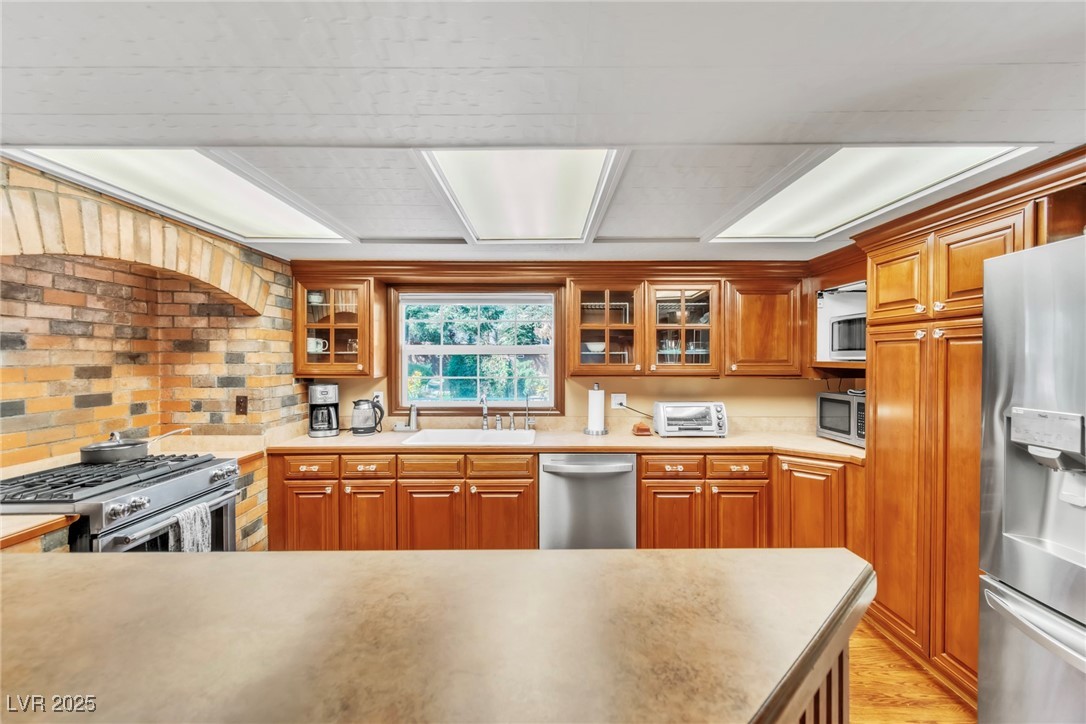 4063 Zugspitz Way Las Vegas, NV 89124 - Photo 56 of 86 Kitchen with stainless steel appliances, brown cabinetry, glass insert cabinets, and light countertops