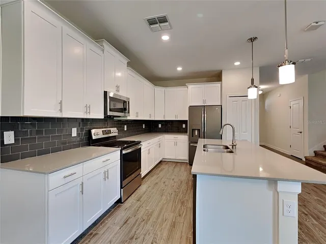 a large kitchen with kitchen island a stove a sink a refrigerator and white cabinets with wooden floor