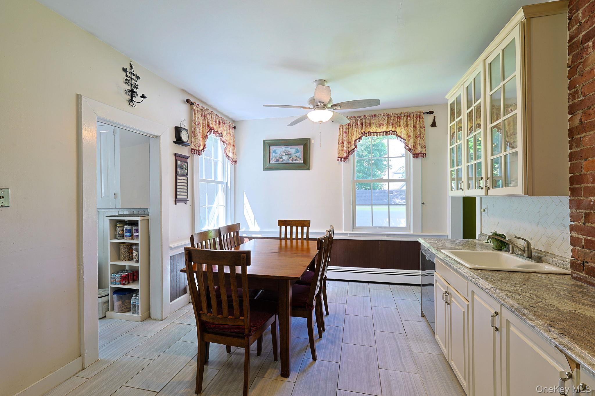 9 Library Road Tuxedo Park, NY 10987 - Photo 11 of 37 Kitchen and dining area featuring light-toned tile flooring, white cabinetry with glass-front uppers, a light-colored countertop, and a built-in sink with a stainless steel faucet