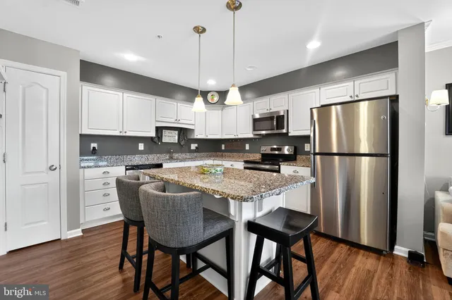 a kitchen with stainless steel appliances granite countertop a refrigerator a stove a sink a microwave and white cabinets with wooden floor