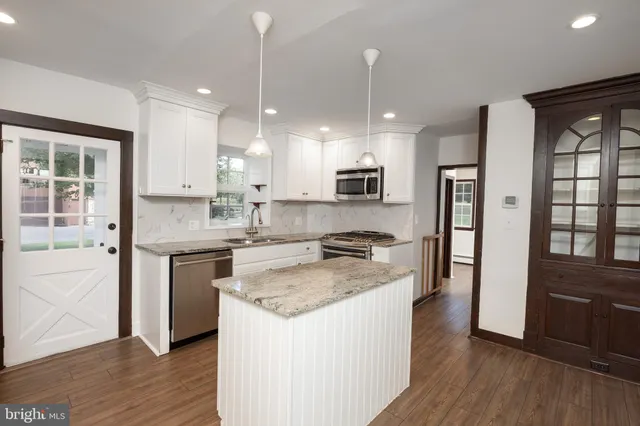 a kitchen with kitchen island granite countertop wooden floors white cabinets and stainless steel appliances