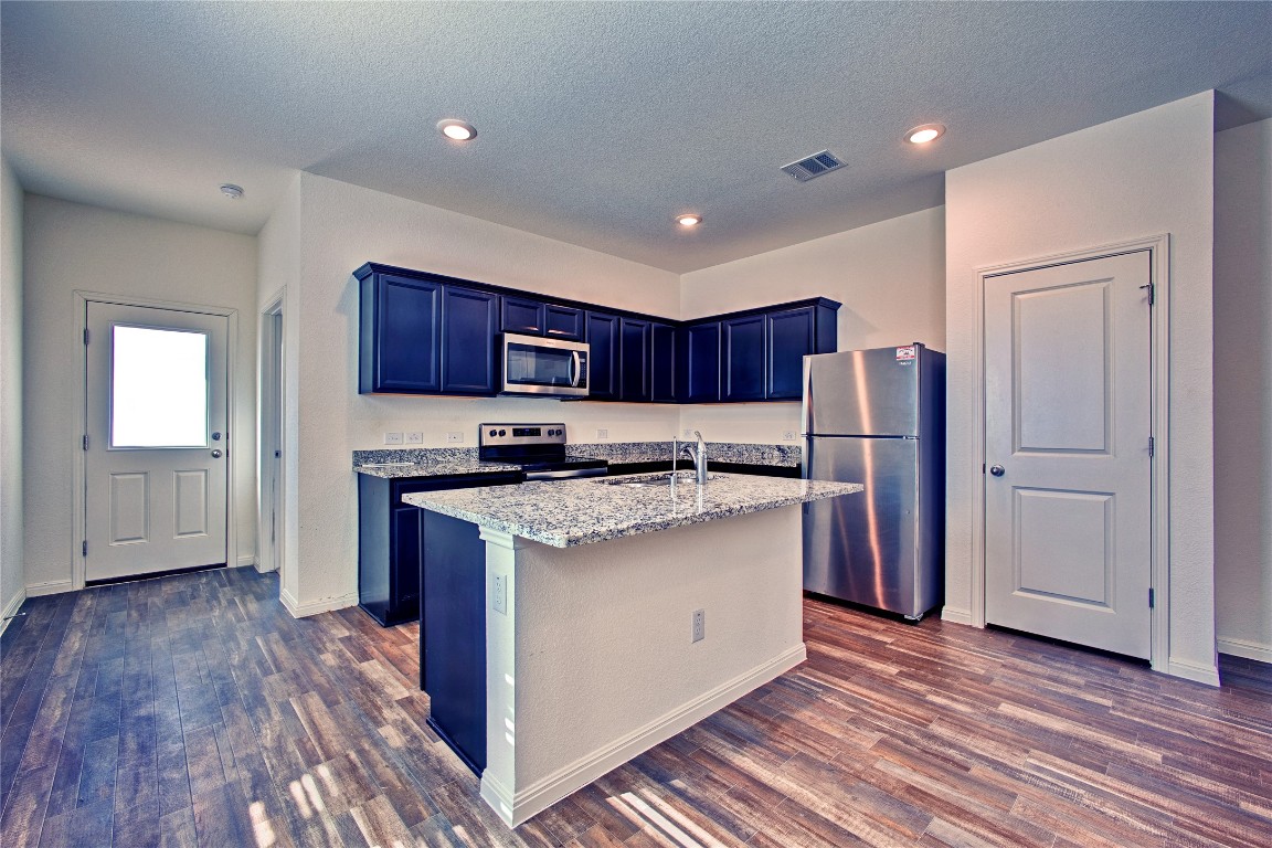 125 Woodpecker Run Jarrell, TX 76537 - Photo 7 of 22 Kitchen with stainless steel appliances, light stone countertops, a kitchen island with sink, dark wood-style flooring, and a textured ceiling