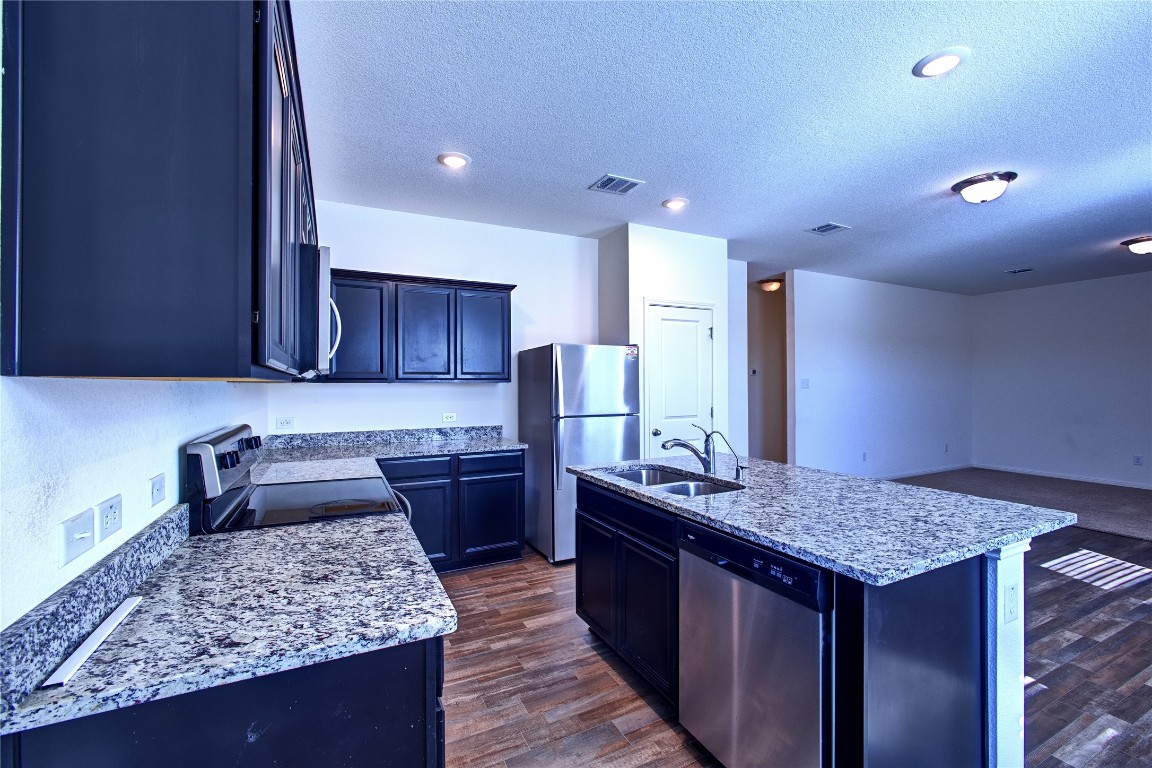 125 Woodpecker Run Jarrell, TX 76537 - Photo 9 of 22 Kitchen featuring appliances with stainless steel finishes, light stone countertops, dark wood-type flooring, a textured ceiling, and a center island with sink