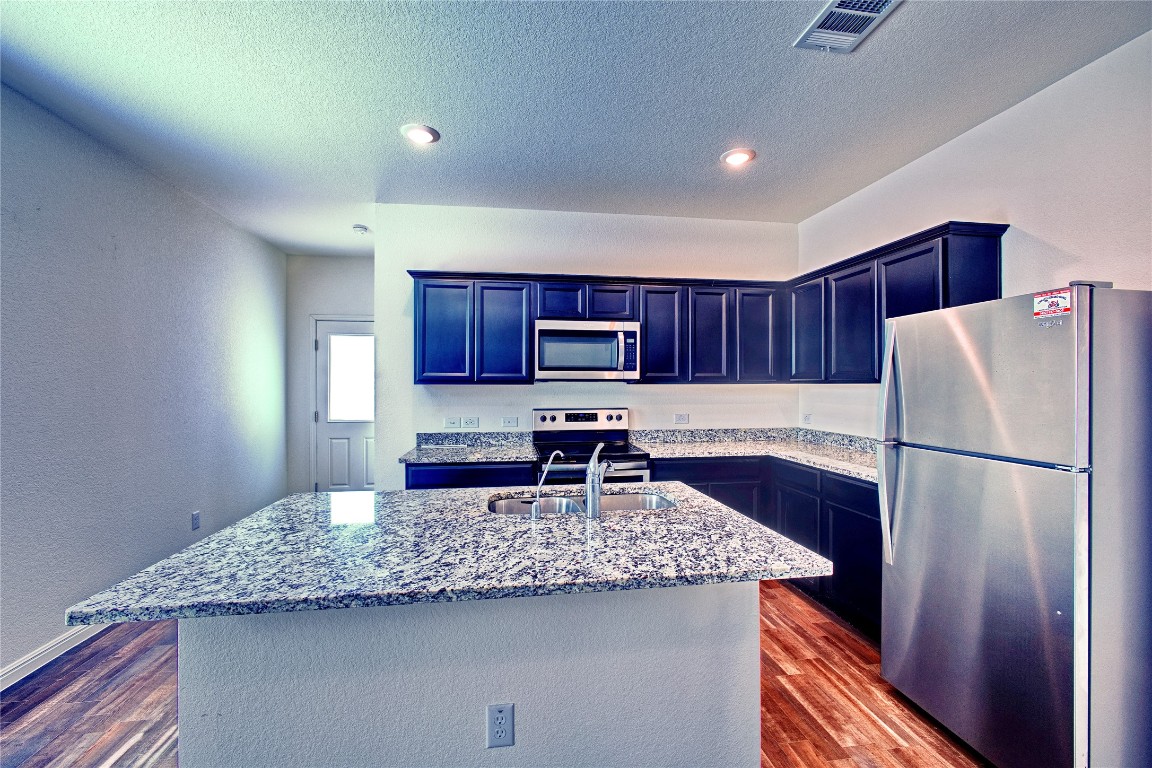 125 Woodpecker Run Jarrell, TX 76537 - Photo 10 of 22 Kitchen with appliances with stainless steel finishes, light stone counters, dark wood-type flooring, an island with sink, and a textured ceiling
