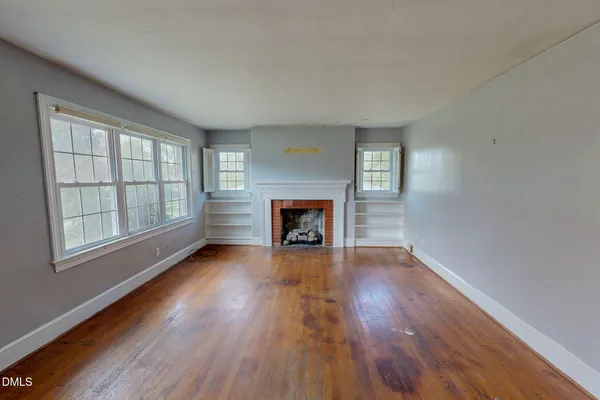 an empty room with wooden floor fireplace and windows
