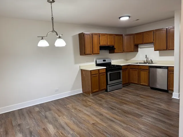 a kitchen with stainless steel appliances granite countertop a sink a stove top oven a chimney wooden floor and cabinets