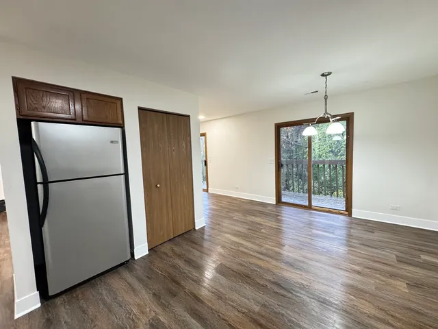 a view of an empty room with wooden floor and a kitchen