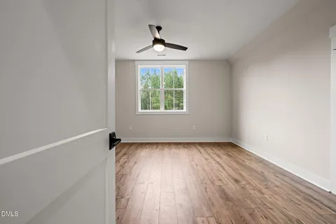 an empty room with wooden floor chandelier fan and windows