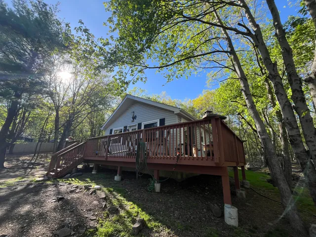 a view of a house with a wooden deck and a forest