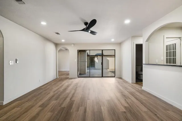 a view of an empty room with wooden floor and a ceiling fan