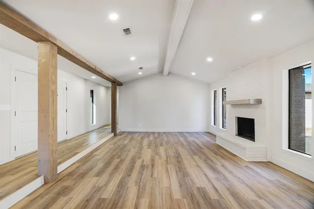 a view of an empty room with wooden floor fireplace and a window