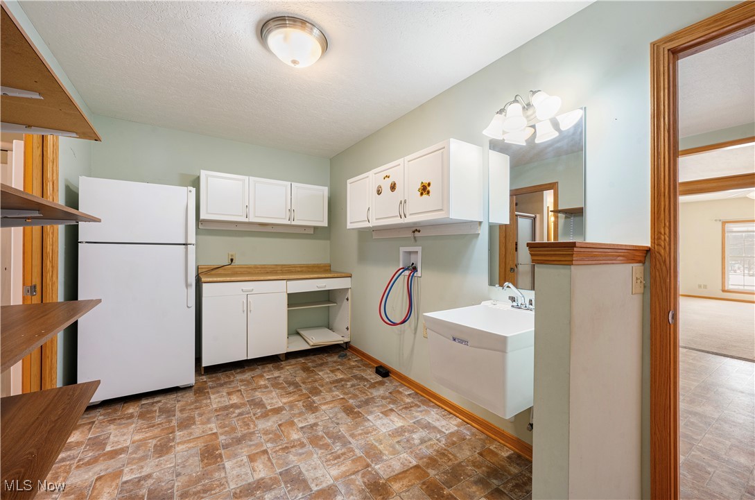 706 Watson Road Deerfield, OH 44411 - Photo 18 of 36 Laundry room featuring white fridge, white cabinetry, and a textured ceiling