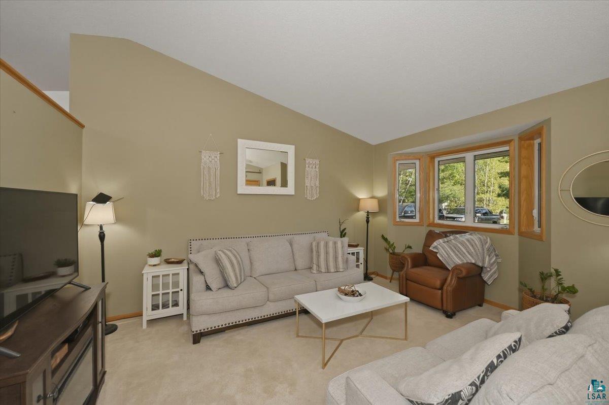 47 Amy Lane Esko, MN 55733 - Photo 7 of 33 Living area featuring vaulted ceilings, a large bay window with wood trim, neutral wall tones, and carpeting