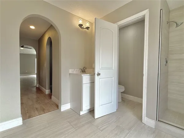 a view of a hallway to an empty room with wooden floor and a bathroom