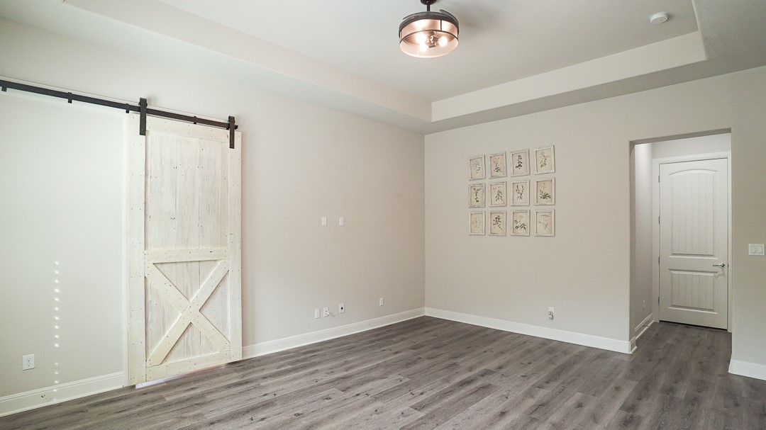 629 Germander Road Leander, TX 78641 - Photo 22 of 32 A spacious room features a trendy barn door, tray ceiling, and durable wood-look flooring.