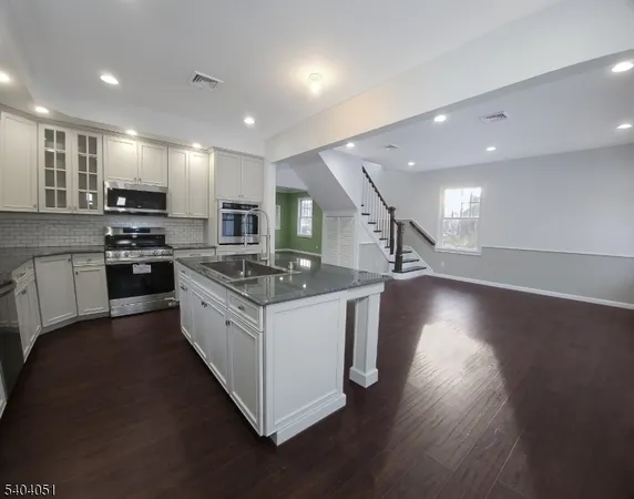 a large white kitchen with stainless steel appliances granite countertop a stove and a wooden floors