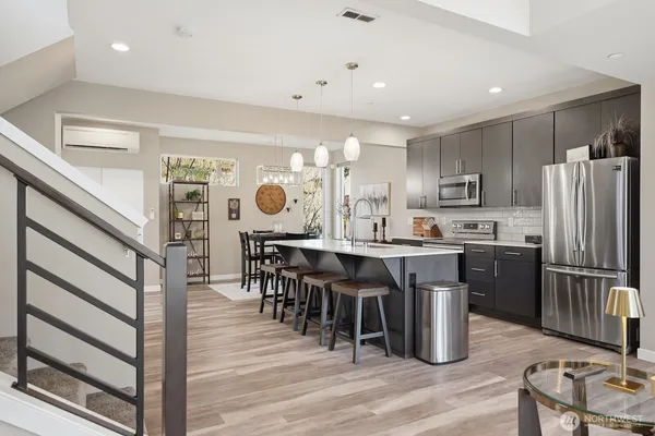 a open kitchen with stainless steel appliances granite countertop a stove top oven a sink dishwasher a dining table and chairs with wooden floor