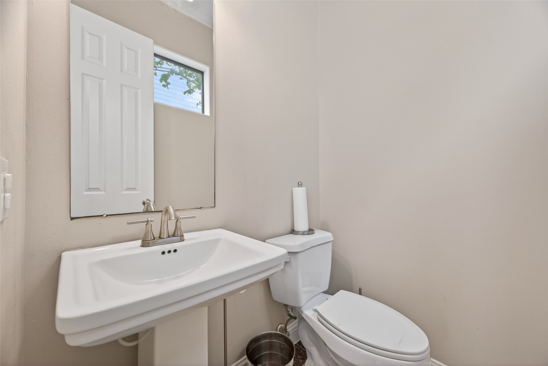 2611 Riverside Drive, Unit C Houston, TX 77004 - Photo 42 of 50 This is a compact, well-lit half bathroom featuring a pedestal sink, modern faucet, and standard toilet. A small window provides natural light, and the neutral color scheme offers a clean, simple look.