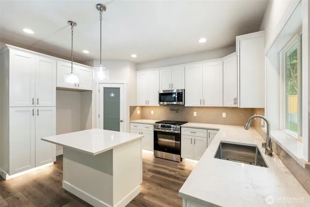 a kitchen with stainless steel appliances a stove a refrigerator a sink and white cabinets with wooden floor