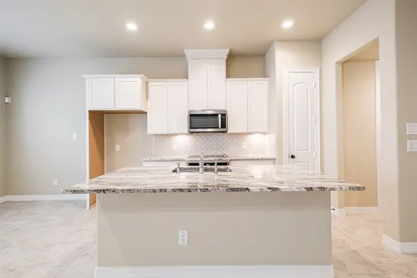 a kitchen with kitchen island granite countertop a stove top oven a sink and white cabinets