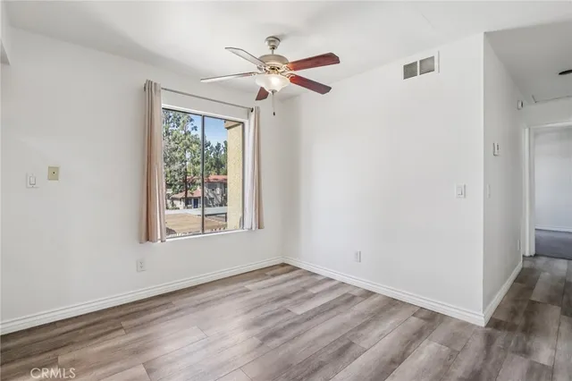 an empty room with wooden floor fan and windows