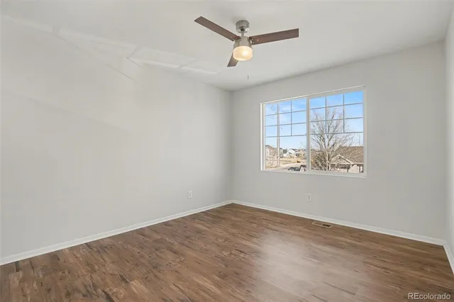 an empty room with wooden floor ceiling fan and windows