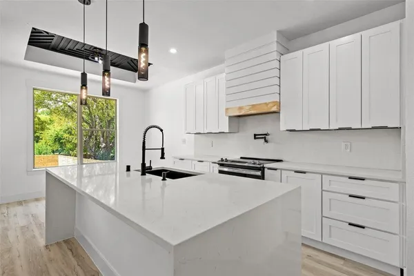 a large white kitchen with kitchen island a refrigerator a stove a sink dishwasher and a oven with wooden floor