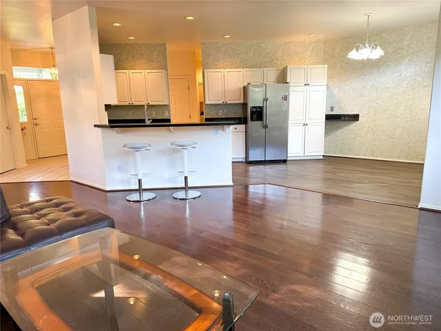 a kitchen with granite countertop a refrigerator a stove top oven and a dining table with wooden floor