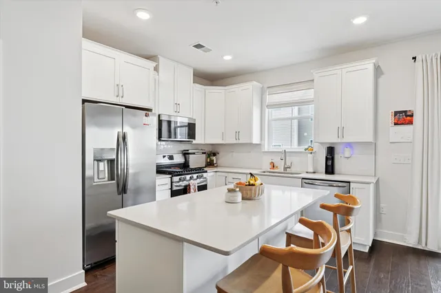 a kitchen with stainless steel appliances a refrigerator a stove a sink dishwasher and white cabinets with wooden floor