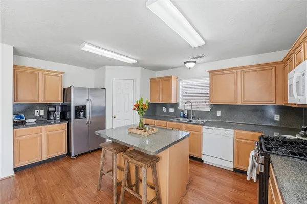 a kitchen with stainless steel appliances granite countertop a stove top oven a refrigerator a sink and dishwasher with wooden floor