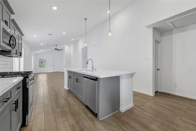 a large kitchen with stainless steel appliances a large counter top a stove a sink and a wooden floors