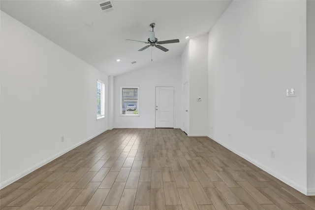 an empty room with wooden floor a ceiling fan and windows