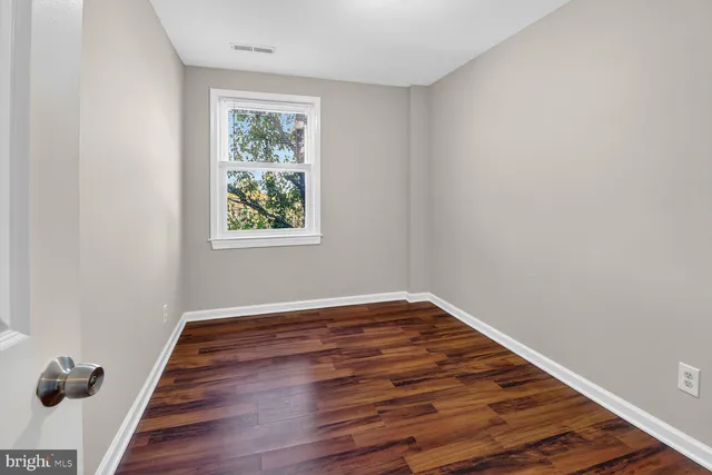 a view of an empty room with wooden floor and a window